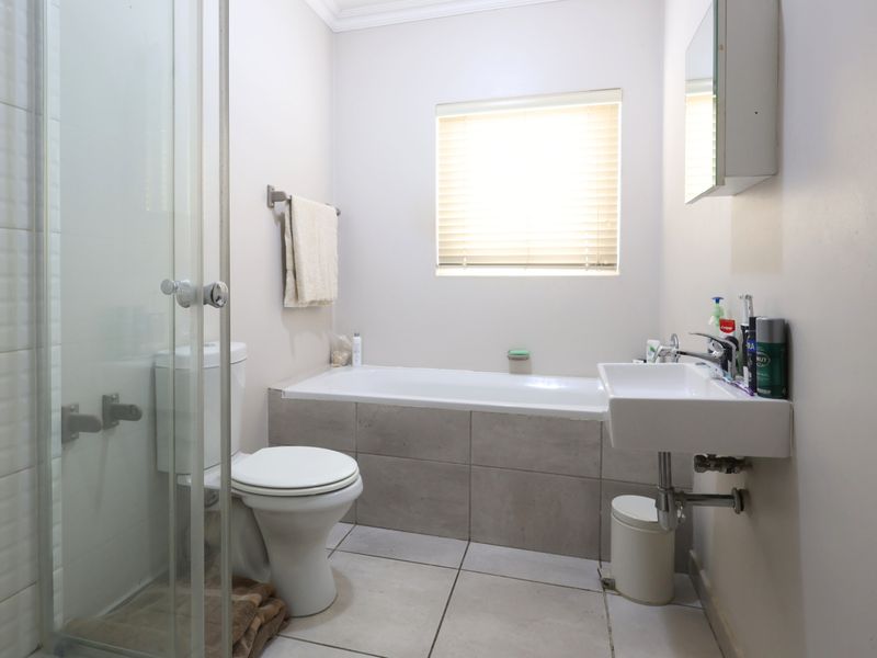 A functional bathroom featuring a shower enclosure, bathtub, wall-mounted basin, and neutral tiled finishes, providing a clean and practical space.