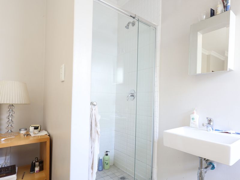 A functional bathroom featuring a glass-enclosed shower with tiled flooring and a modern wall-mounted basin with chrome fixtures.