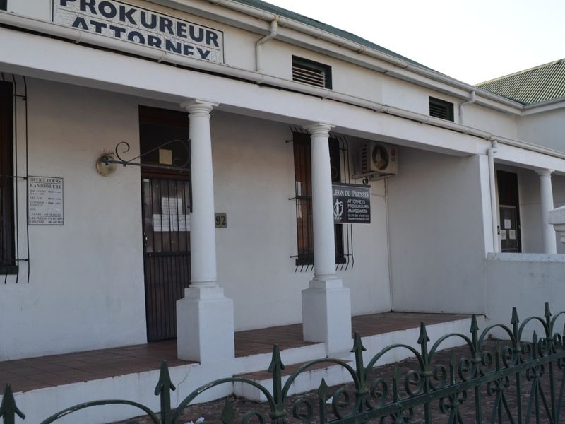 Front facade of a professional office building featuring a covered veranda with classical columns, security bars, and street-facing signage.