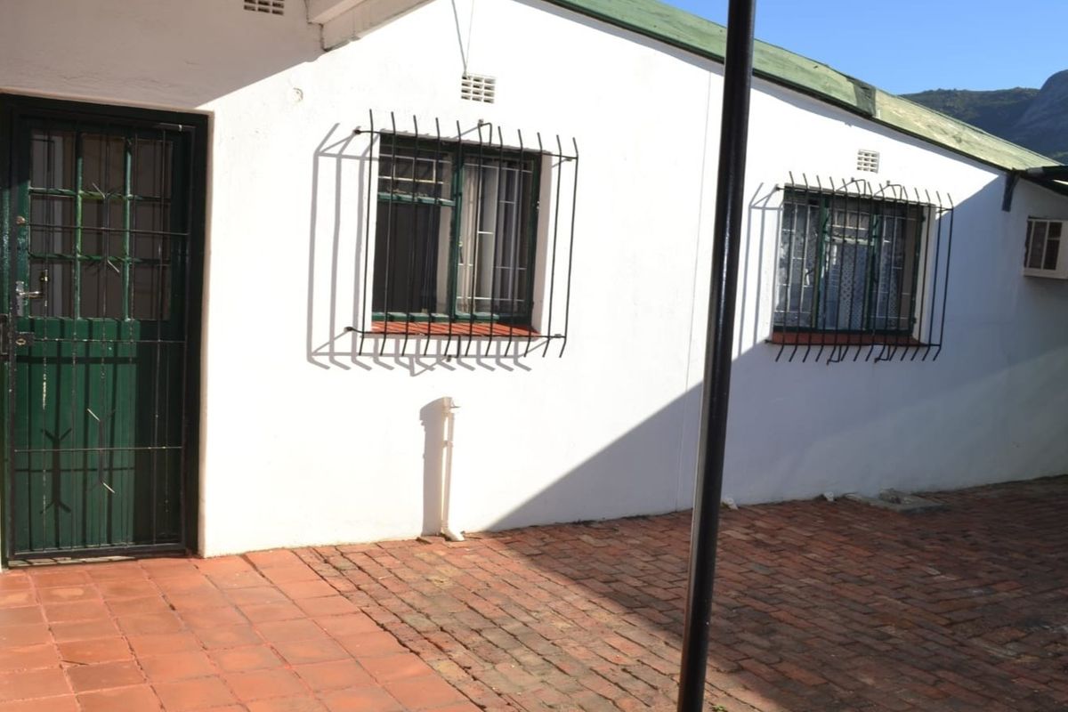 Rear exterior view of the office building featuring brick paving, security bars on windows, and a wall-mounted air conditioning unit.