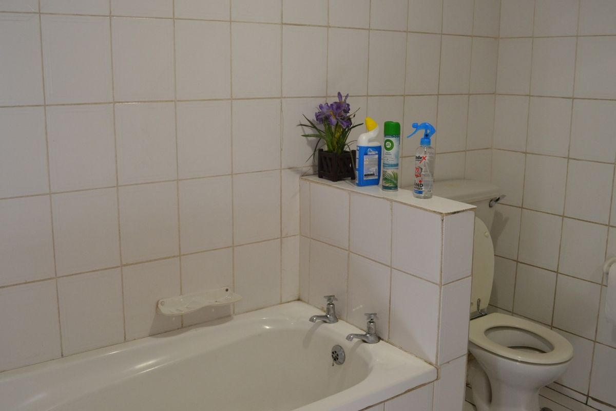 A functional bathroom featuring a built-in bathtub and toilet, finished with white ceramic wall tiles and a half-wall partition.