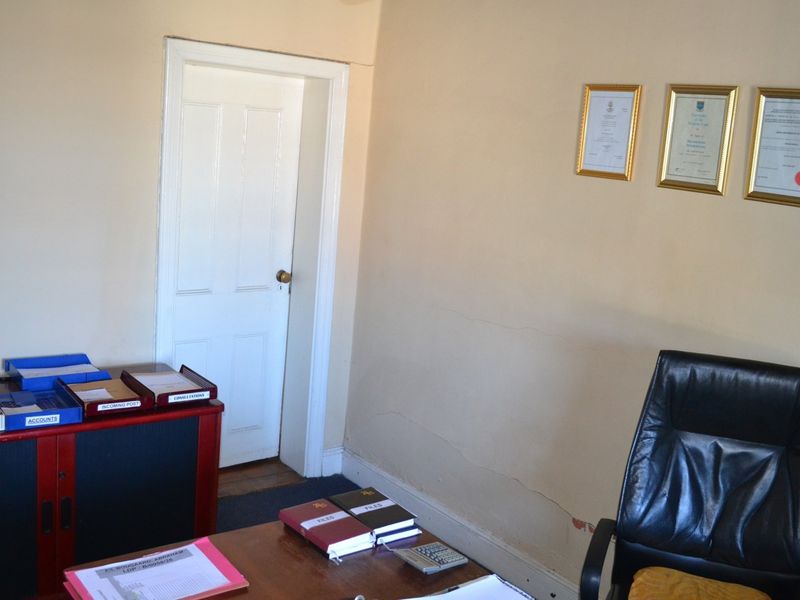 A functional office space featuring a classic timber door and wall-mounted display frames, currently showing signs of wear including cracked plaster and peeling paint.
