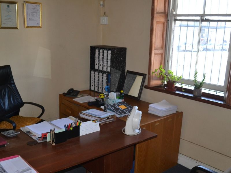 A functional office space featuring a timber-framed window with security bars and neutral wall finishes.