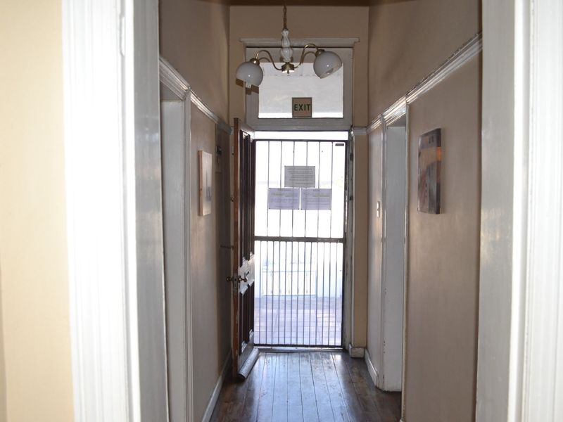 A narrow office hallway featuring timber flooring, picture rails, and a secure metal entrance gate with a transom window above.