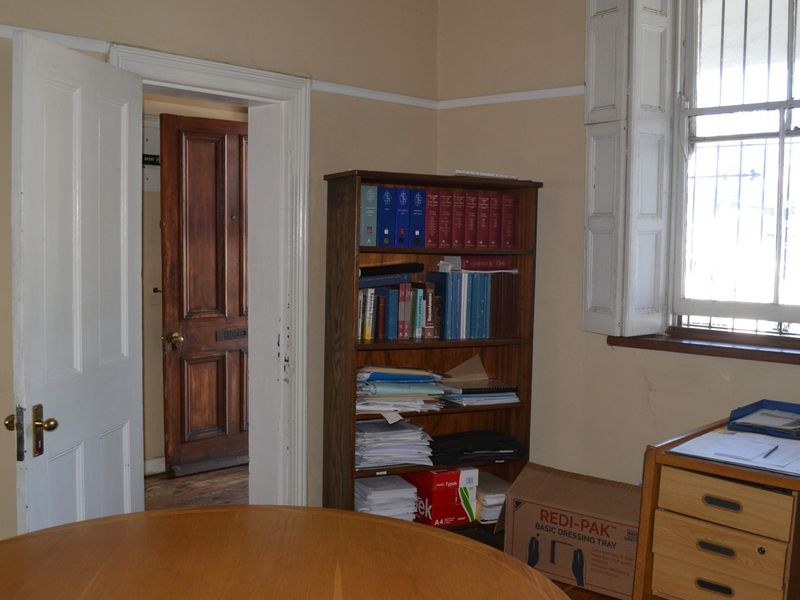 A functional office space featuring traditional timber doors, window shutters with security bars, and classic picture rails, requiring some cosmetic maintenance.