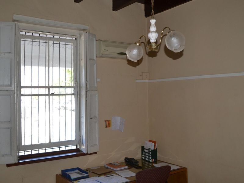 A functional office space featuring exposed timber ceiling beams, a split-system air conditioner, and a window fitted with security bars and timber shutters.