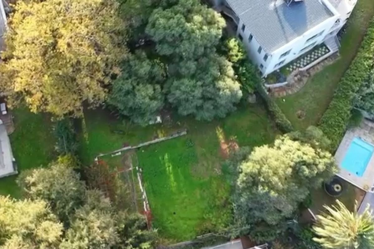 An aerial view of the property grounds, showcasing the landscaped garden, mature trees, and a swimming pool area.