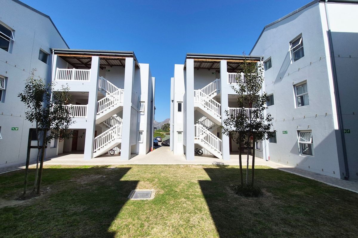 Exterior view of apartment complex buildings featuring central lawn, paved walkways, and external staircases leading to upper-level balconies.