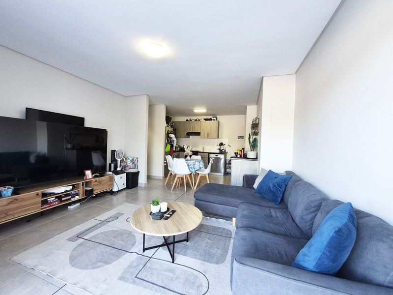 Open-plan living and dining area featuring tiled floors and a functional kitchen with built-in cabinetry and appliances.