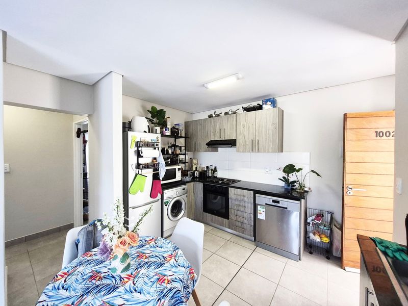 Compact kitchen featuring wood-look cabinetry, tiled flooring, built-in oven, hob, extractor fan, and integrated space for a washing machine.