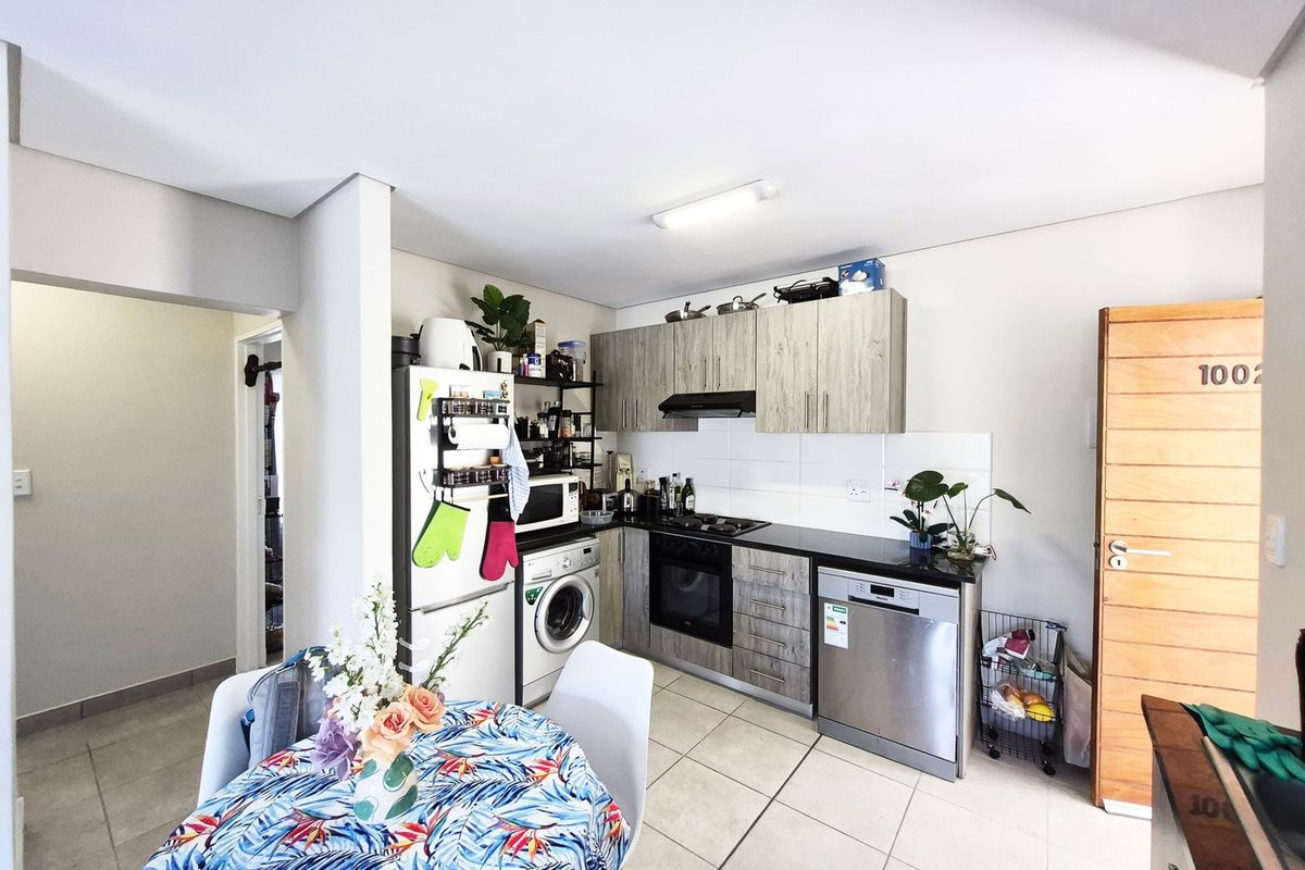 Compact kitchen featuring wood-look cabinetry, tiled flooring, built-in oven, hob, extractor fan, and integrated space for a washing machine.