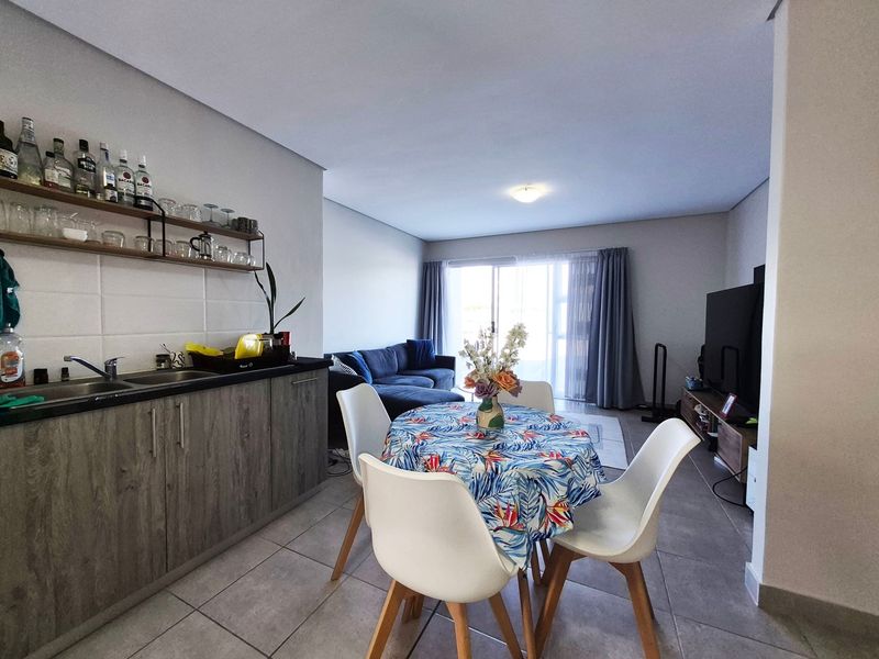Open-plan living and dining area featuring tiled flooring, a compact kitchen with modern cabinetry, and a sliding glass door leading to the exterior.