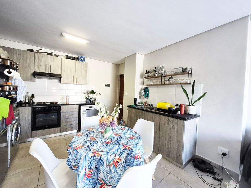 Open-plan kitchen and dining area featuring wood-look cabinetry, built-in oven and hob, tiled backsplash, and neutral floor tiles.