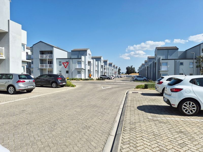 Exterior view of a modern apartment complex featuring paved parking areas and multi-story residential buildings with balconies.
