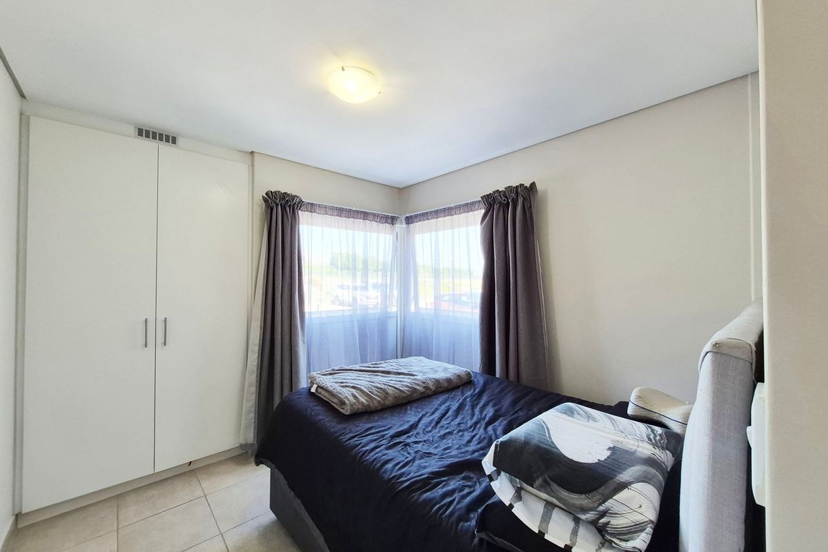 A bright bedroom featuring built-in wardrobes, tiled flooring, and corner windows that allow for natural light.