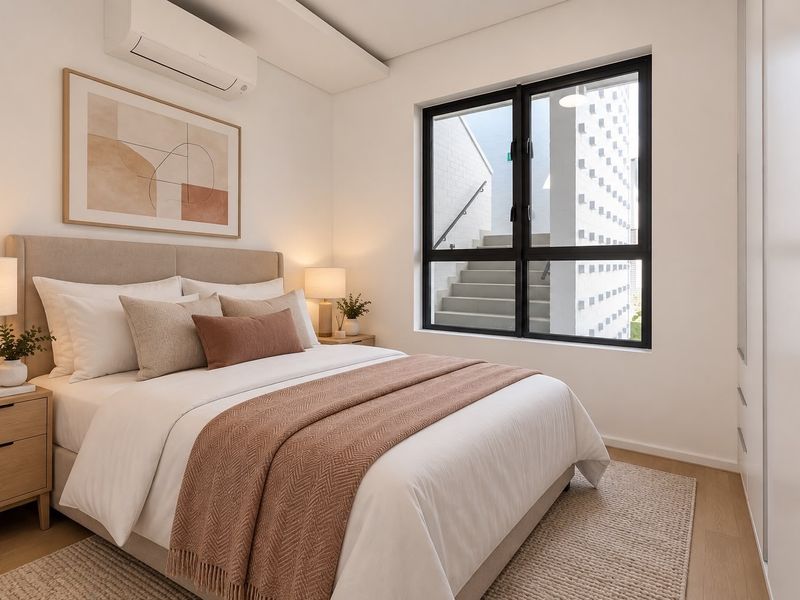 A modern, well-maintained bedroom featuring a split-system air conditioner, built-in wardrobe, and large window with views of the exterior staircase.