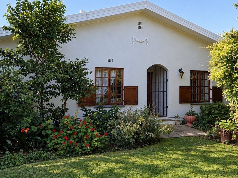 Charming front facade featuring white rendered walls, timber-framed windows with shutters, and a secure arched entrance set within a well-maintained garden.