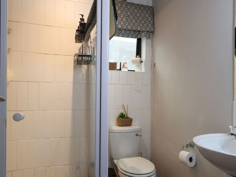 A functional bathroom featuring a shower enclosure with tiled walls, a standard toilet, and a pedestal basin with a modern mixer tap.