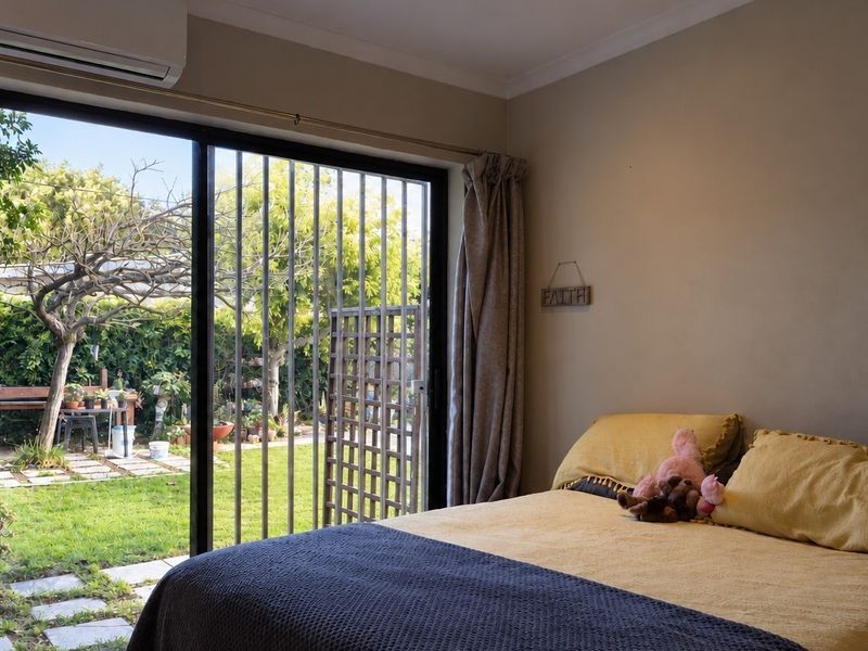 A bedroom featuring a sliding glass door with security gate, providing direct access to the rear garden and equipped with a wall-mounted air conditioner.