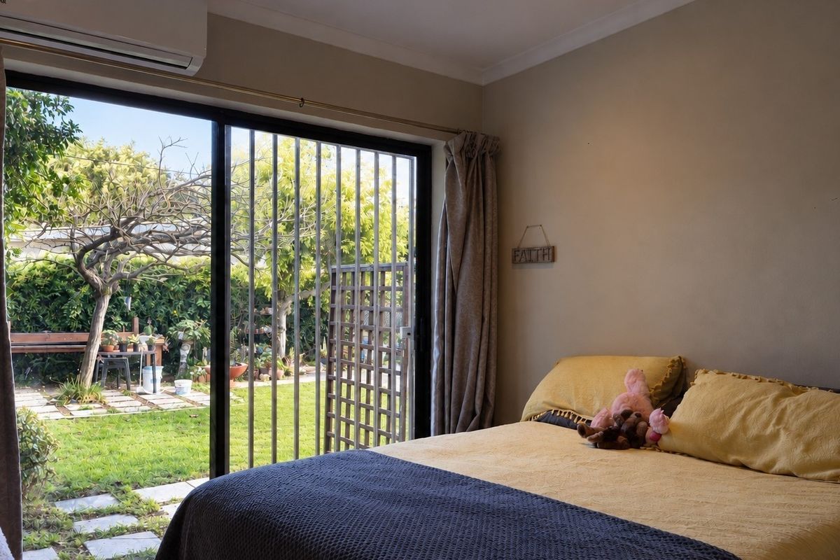 A bedroom featuring a sliding glass door with security gate, providing direct access to the rear garden and equipped with a wall-mounted air conditioner.