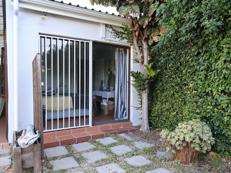 Rear exterior view featuring a sliding glass door with security gate, tiled threshold, and paved patio area adjacent to a garden space.