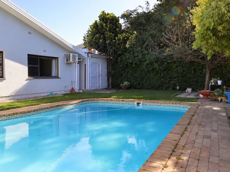 A backyard pool area featuring a swimming pool with brick coping, surrounding brick paving, and a well-maintained lawn area.