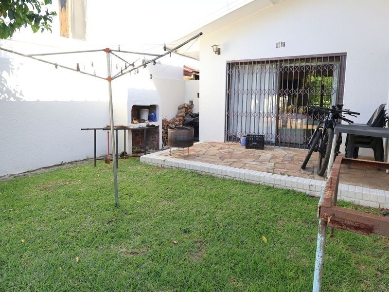 Rear garden area featuring a stone-paved patio, built-in braai, and sliding door access to the home.