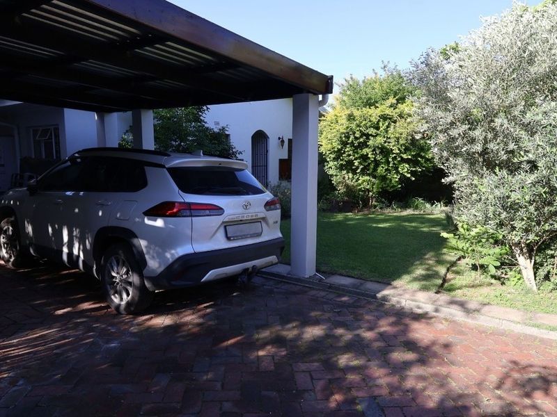 A covered carport area with a brick-paved driveway and an adjacent well-maintained garden space.