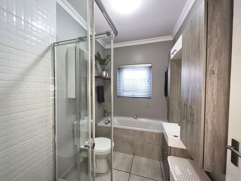 Modern bathroom featuring a glass shower enclosure, built-in bathtub, and contemporary wood-finish vanity cabinetry with integrated storage.