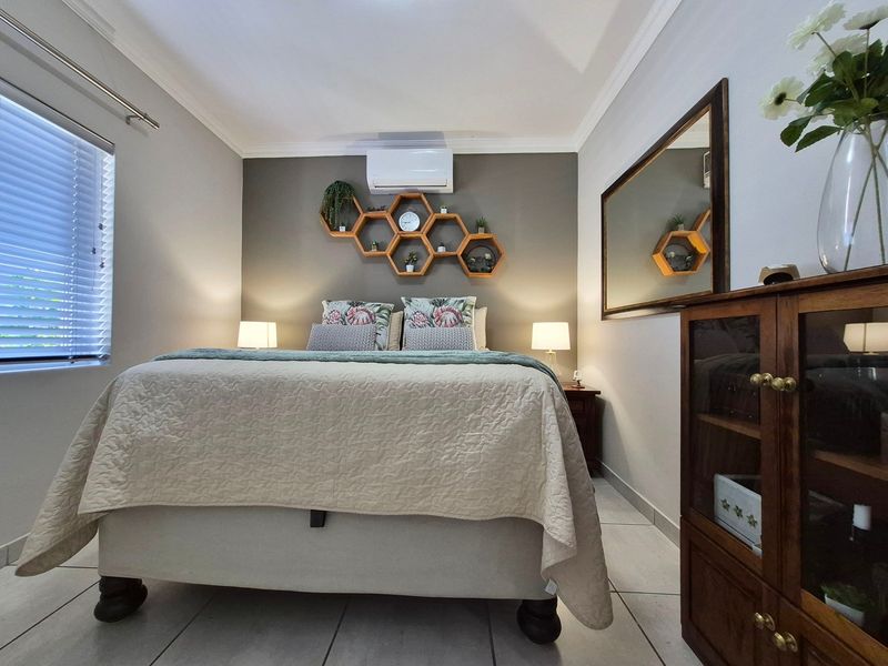 A well-maintained bedroom featuring tiled flooring, crown molding, venetian blinds, and a wall-mounted air conditioning unit.