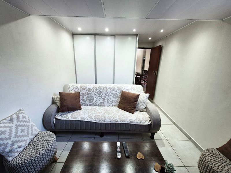 A compact living room featuring tiled flooring, recessed ceiling lighting, and a large built-in sliding door wardrobe for storage.