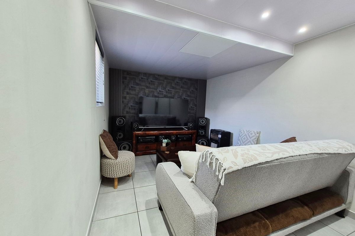A comfortable living room featuring tiled flooring, recessed downlighting, and a textured feature wall, creating a functional and inviting space.