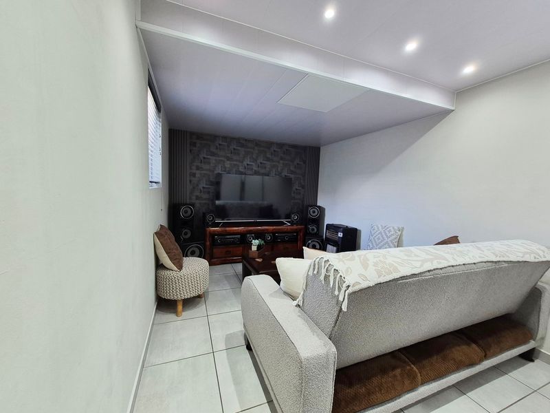 A comfortable living room featuring tiled flooring, recessed downlighting, and a textured feature wall, creating a functional and inviting space.