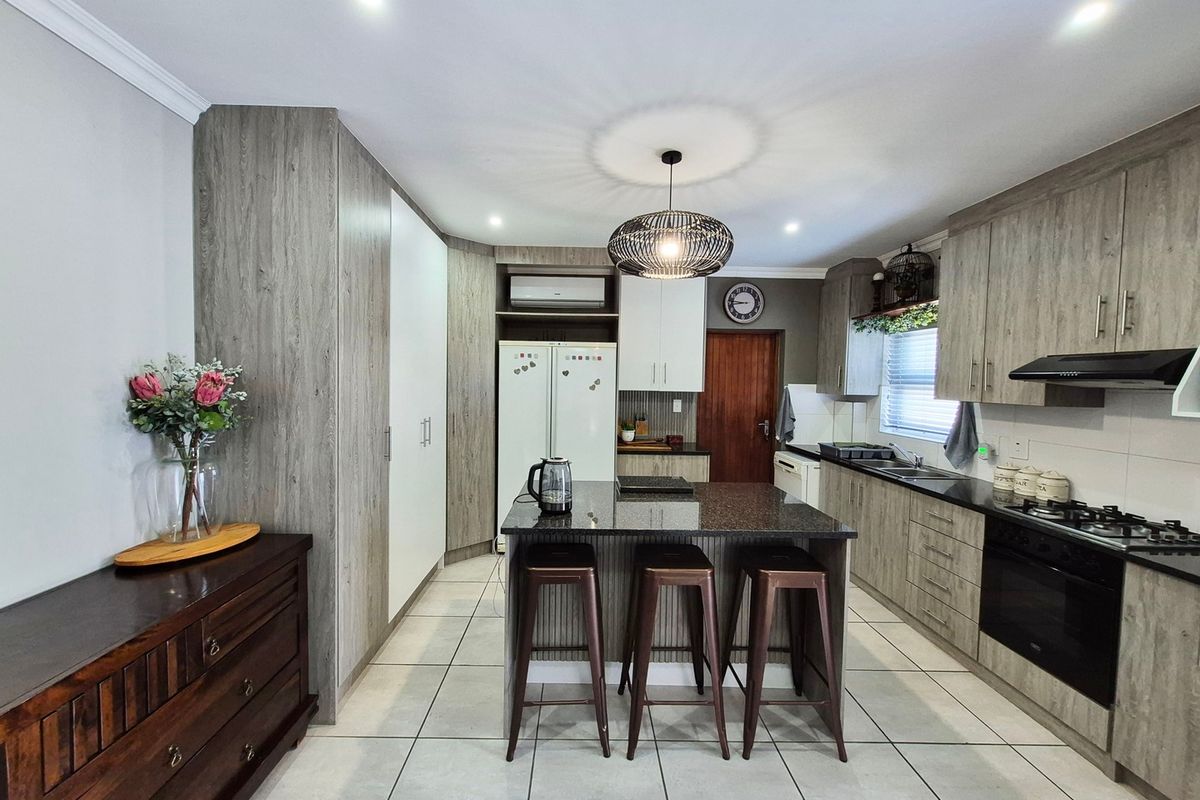 Modern kitchen featuring wood-grain cabinetry, granite countertops, a central island with breakfast bar, built-in oven, gas hob, and tiled flooring.