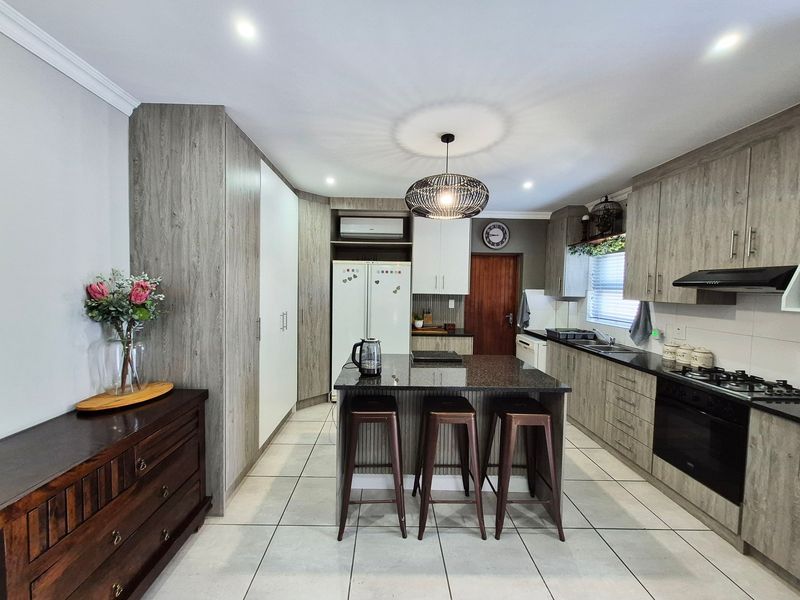 Modern kitchen featuring wood-grain cabinetry, granite countertops, a central island with breakfast bar, built-in oven, gas hob, and tiled flooring.