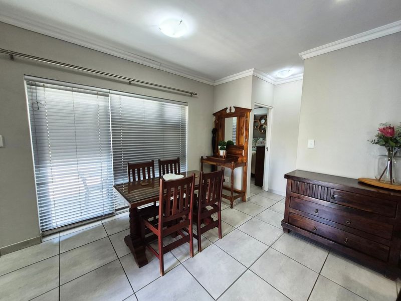 A bright dining area featuring neutral tiled flooring, ceiling cornices, and a large sliding glass door with venetian blinds providing natural light.