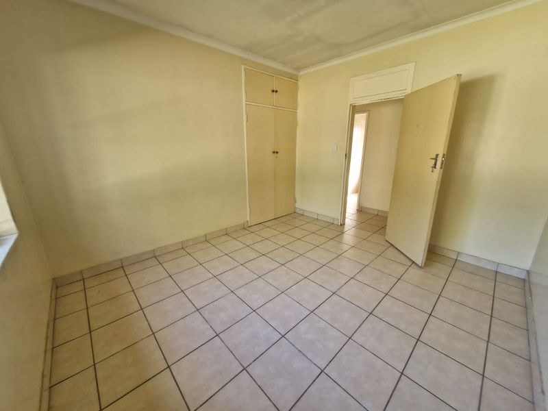 An empty bedroom featuring tiled flooring, built-in cupboards, and neutral wall finishes, offering a blank canvas for renovation or interior design updates.