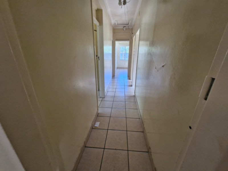 A narrow interior hallway featuring tiled flooring and multiple doorways, currently showing signs of wear and requiring cosmetic updates to the wall finishes.