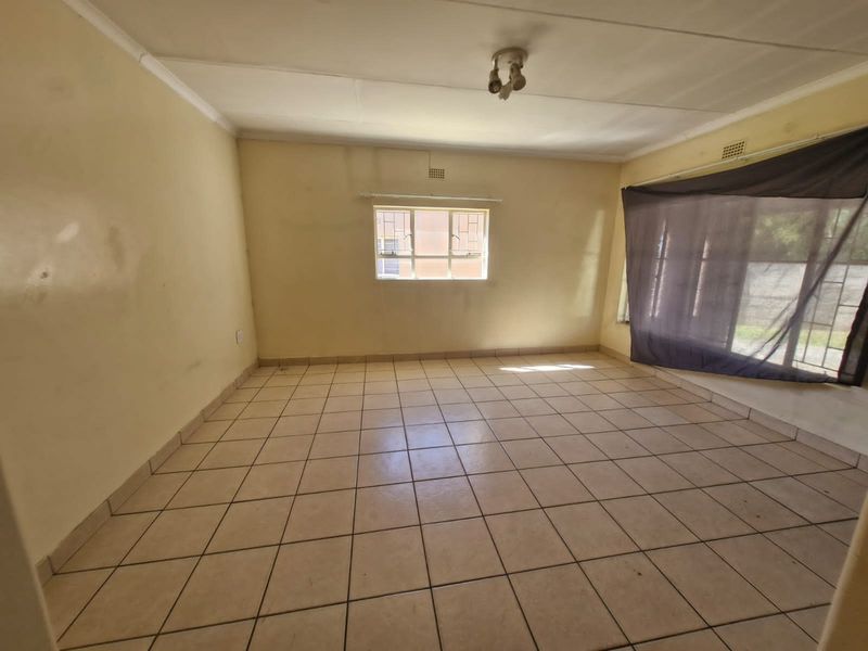 An empty living room featuring tiled flooring, a ceiling light fixture, and a sliding door leading to the exterior.