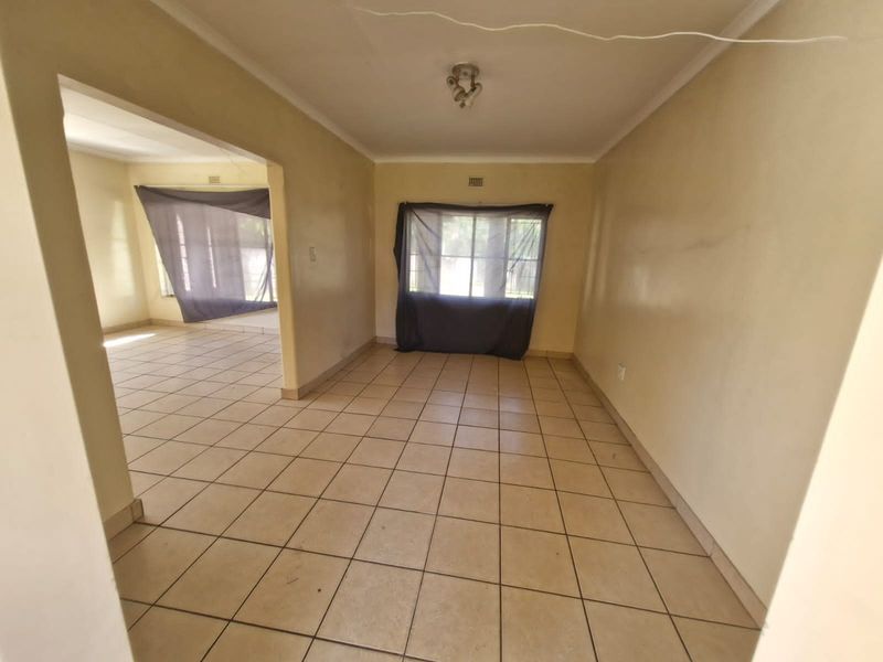 An empty open-plan living area featuring ceramic floor tiles, neutral wall finishes, and window security bars, offering a blank canvas for renovation.