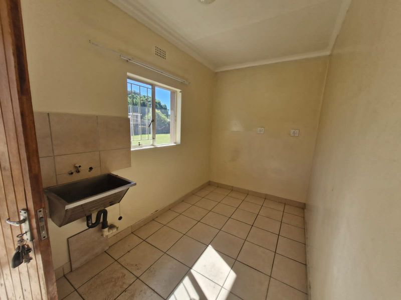 A functional laundry room featuring a stainless steel utility sink, tiled flooring, and plumbing connections, ready for modernization.