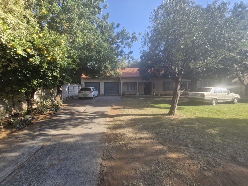 Front view of a residential property featuring a concrete driveway, double garage, and a spacious front garden with mature trees.