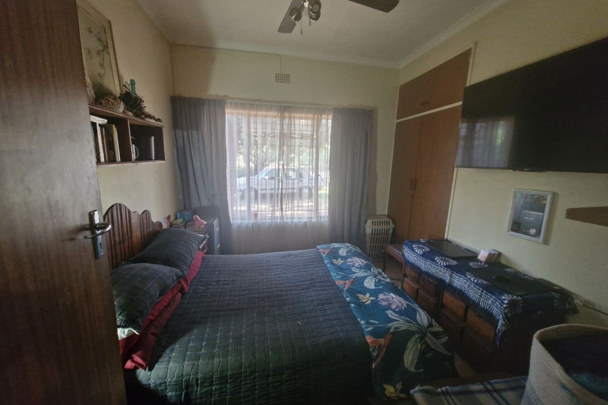 A functional bedroom featuring built-in cupboards, a ceiling fan, and natural light through a large window.