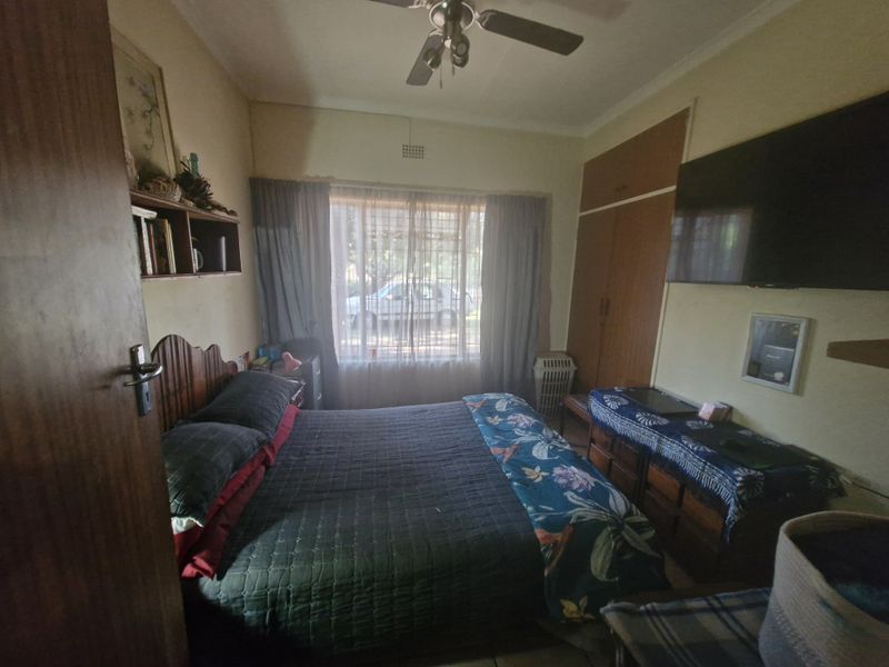 A functional bedroom featuring built-in cupboards, a ceiling fan, and natural light through a large window.