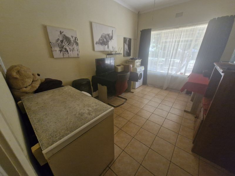 A multi-purpose utility room featuring tiled flooring and a large window, currently utilized as a workspace and storage area.