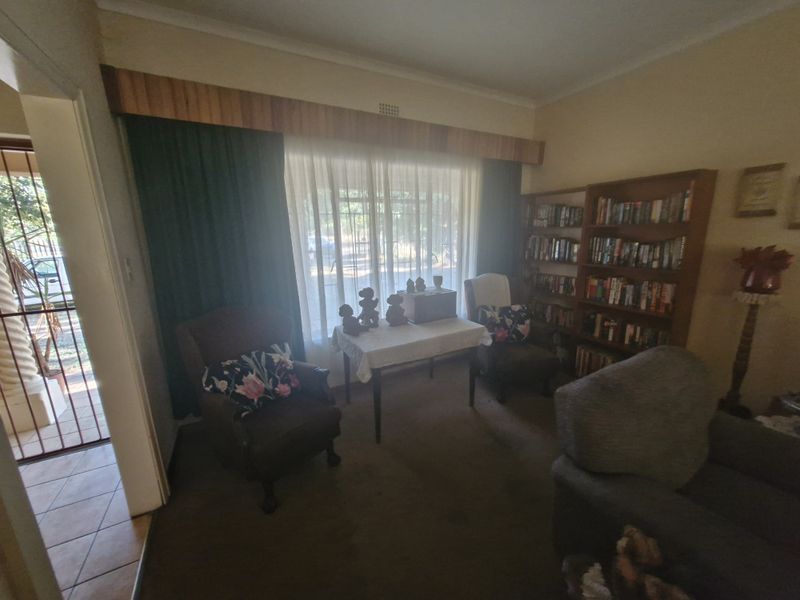A living room featuring a built-in bookshelf, wooden pelmet, and carpet flooring, offering a cozy space with potential for modernization.