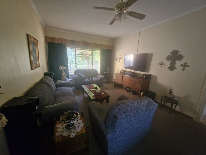A comfortable living room featuring a ceiling fan and large window with security bars, providing a functional and lived-in space.