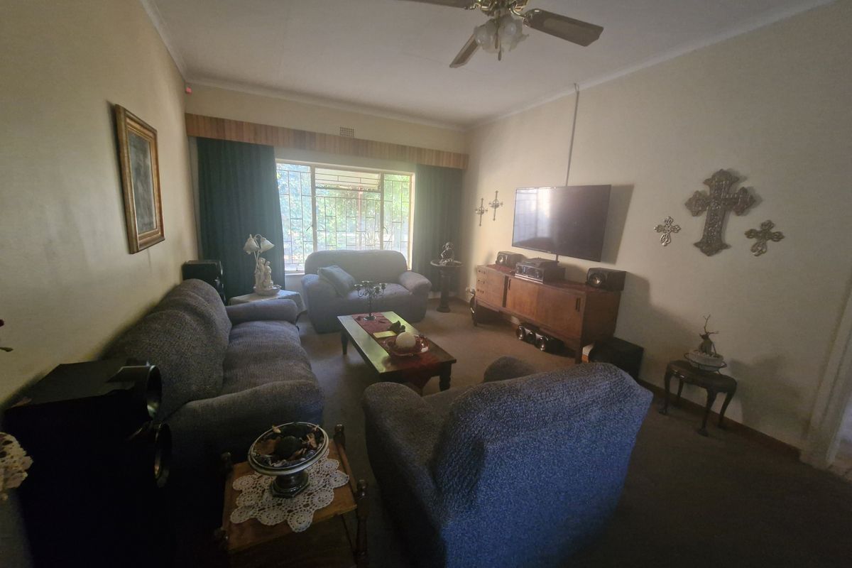 A comfortable living room featuring a ceiling fan and large window with security bars, providing a functional and lived-in space.