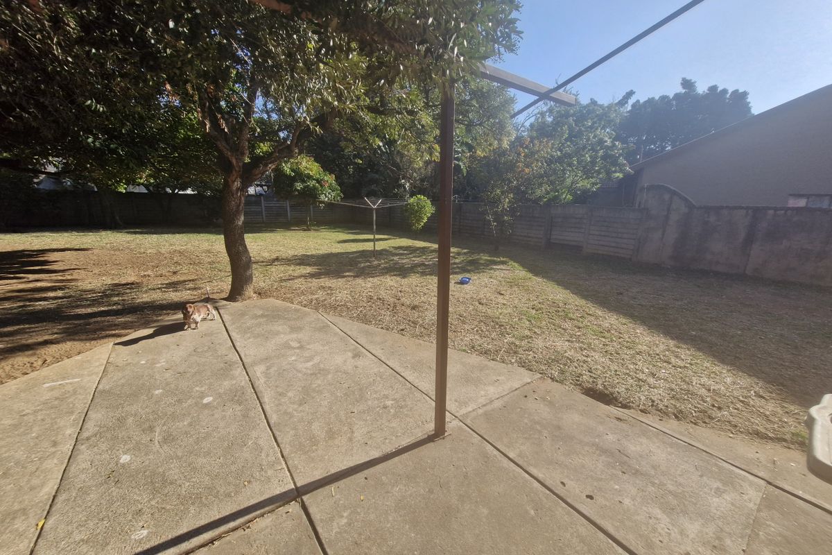 A spacious rear garden featuring a concrete patio area, a metal pergola frame, and a perimeter wall, offering potential for landscaping and outdoor living.