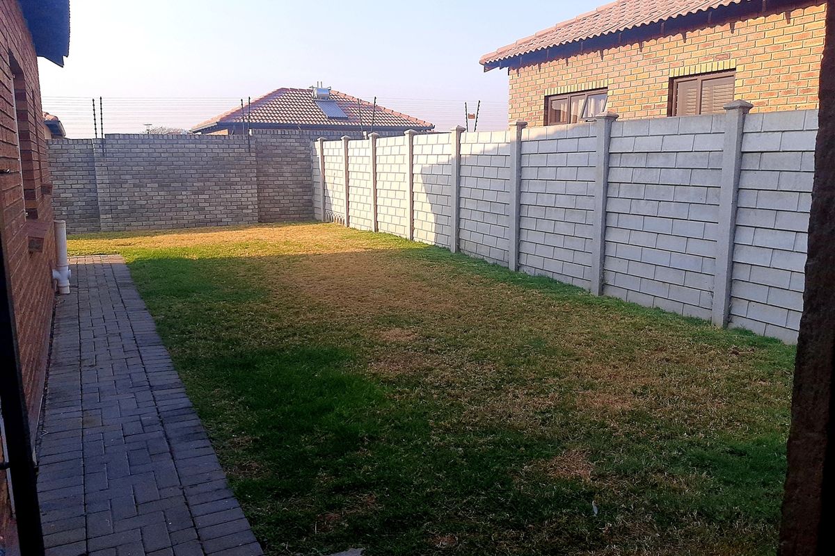 A private rear garden featuring a paved walkway, a grass lawn, and perimeter concrete block wall fencing.